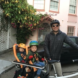 Xtracycle Electric cargo bike with two orange Yepp seats on back and brown walnut wood front coff...